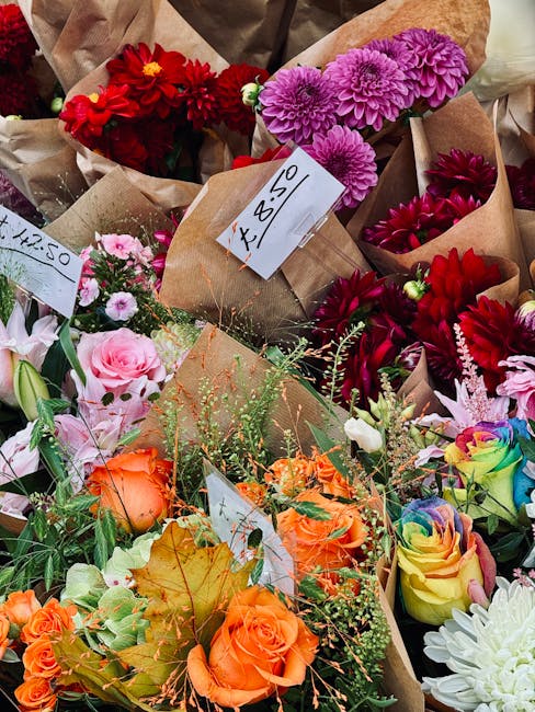 A vibrant display of fresh flower bouquets arranged in brown paper wrapping, featuring a variety of blooms including vivid red dahlias, purple chrysanthemums, soft pink roses, orange roses, rainbow-co